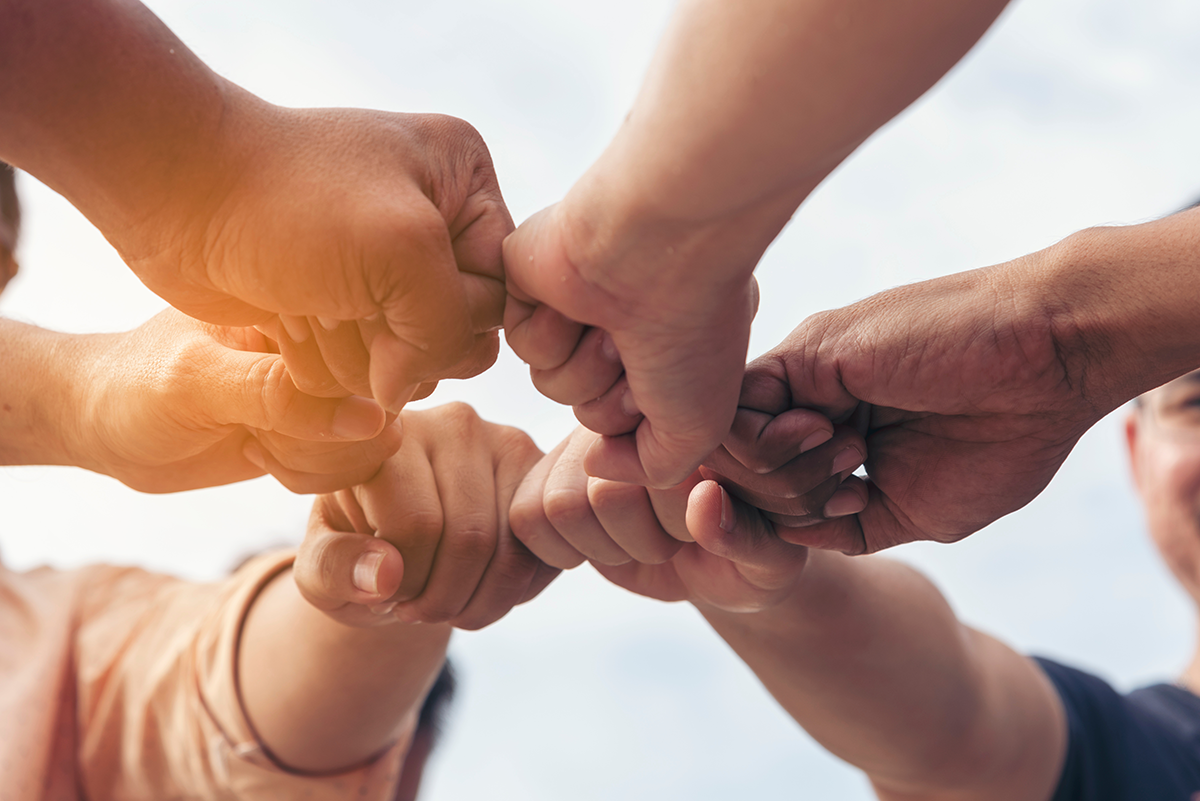 Six hands fist bumping creating a circle photographed from below.